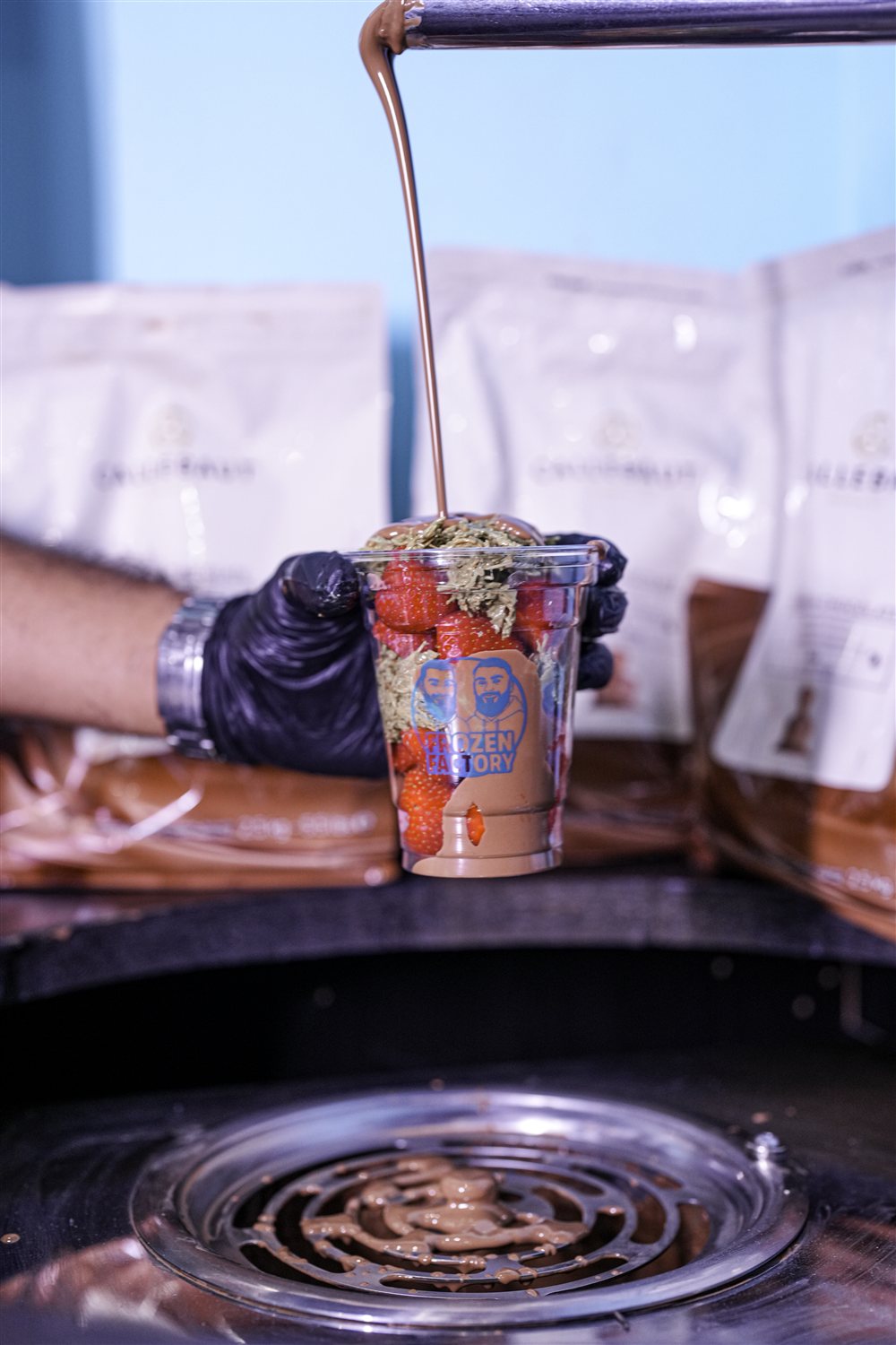 Melted chocolate being poured over a strawberry and kunafa Frozen Factory cup
